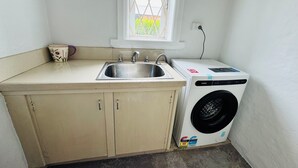Une petite buanderie équipée d’un lave-linge, d’un évier et d’une fenêtre.