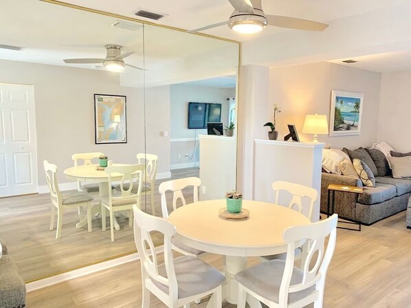 Una sala de estar moderna con una mesa de comedor redonda, sillas blancas, un sofá gris y un ventilador de techo.