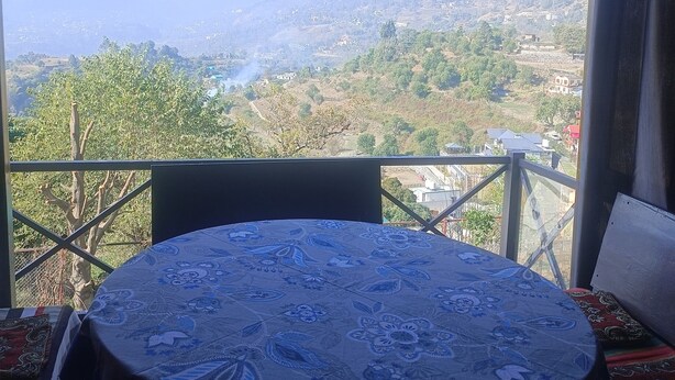 Una mesa redonda con mantel floral, vista a un paisaje montañoso y barandilla de balcón.