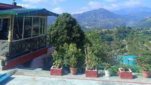 Un edificio con cerramiento de vidrio y tejado rojo, rodeado de plantas en macetas y un paisaje montañoso.