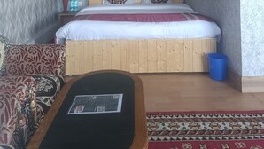Un dormitorio con una cama de madera, un ventilador de techo, un televisor montado en la pared y una alfombra estampada.