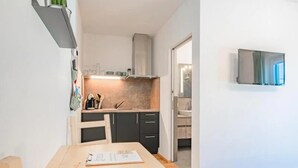 Kompakti keittiö, jossa on puinen pöytä ja tuolit, sisäänrakennettu uuni ja seinälle asennettu televisio.