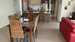 A modern kitchen with white cabinets, a dining area with a wooden table and wicker chairs, and a red sofa in the living area. - Searenity only 750 m to the beach, pet friendly (St Leonards)