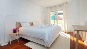 Ein Schlafzimmer mit einem großen Bett, einem Nachttisch, einem Schreibtisch und einem Fenster mit Vorhängen.