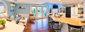 A modern kitchen with a central island, a dining area with a striped sofa, and a view of the outdoors through large sliding doors.