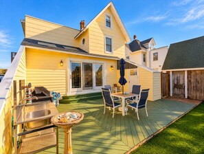 A house with a deck, outdoor grill, and a dining area with chairs and a table.