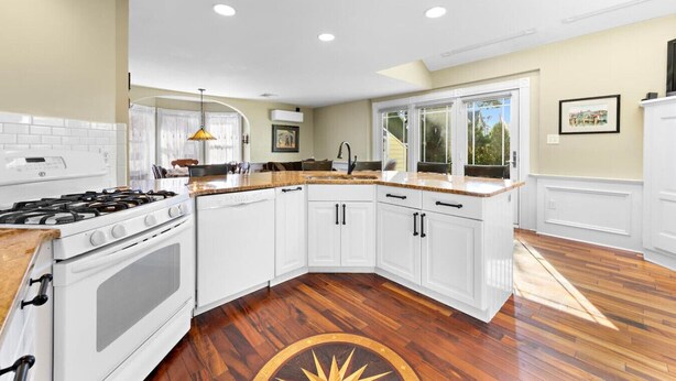 Una cocina moderna con armarios blancos, estufa a gas y piso de madera.