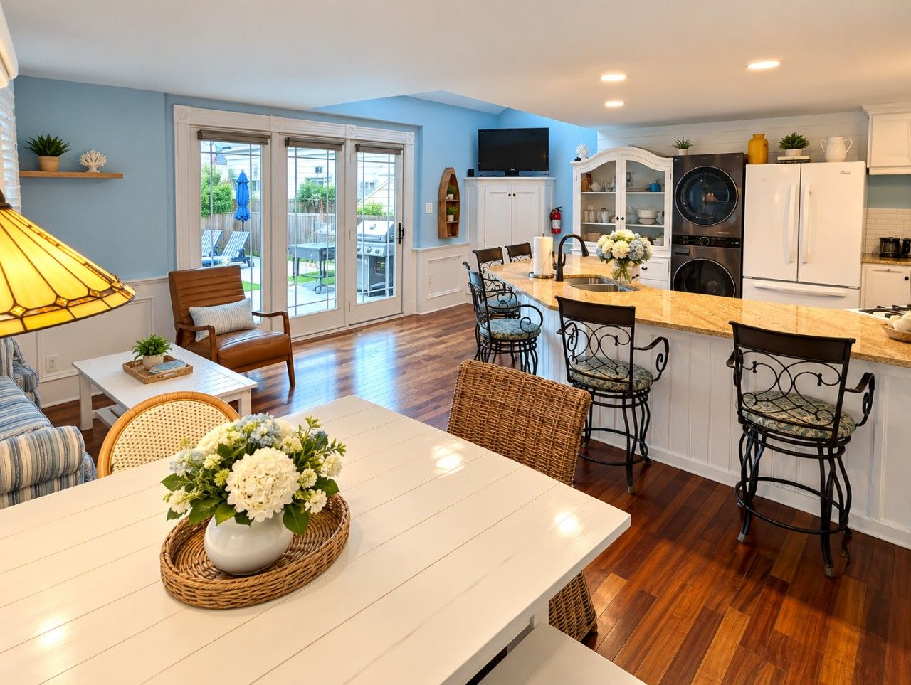 A modern kitchen with a dining area, featuring a central island, bar stools, and a large window.