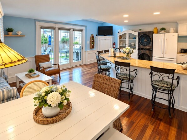 A modern kitchen with a dining area, featuring a central island, bar stools, and a large window.