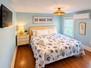 A bedroom with a bed, bedside tables, a lamp, a 'NO WAKE ZONE' sign, and a window with blinds.