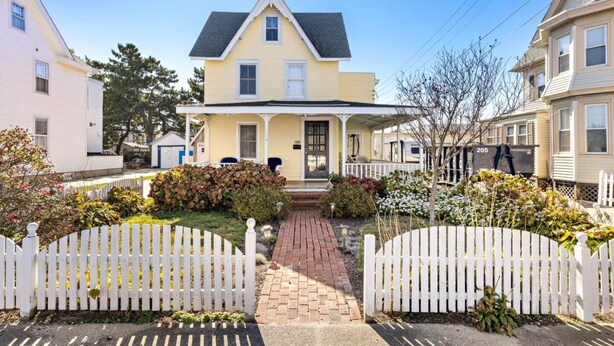 A two-story house with a front porch, a driveway, and a white picket fence.