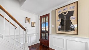 Un pasillo con una escalera de madera, paredes blancas y una fotografía grande en el marco.