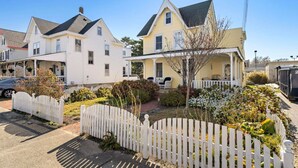 A residential neighborhood with two houses, one white and one yellow, featuring front porches and a picket fence.
