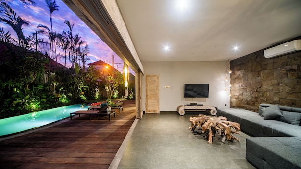 An indoor living area with a stone wall, a wooden coffee table, a sofa, and a TV. - Luxury-3BedRoom-Sang Villa-Central Sanur (Bali)