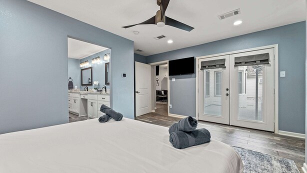 A bedroom with a large bed, a ceiling fan, a walk-in closet, and a bathroom with a mirror and sink. - Luxurious Home with Great Pool Area (Willis)