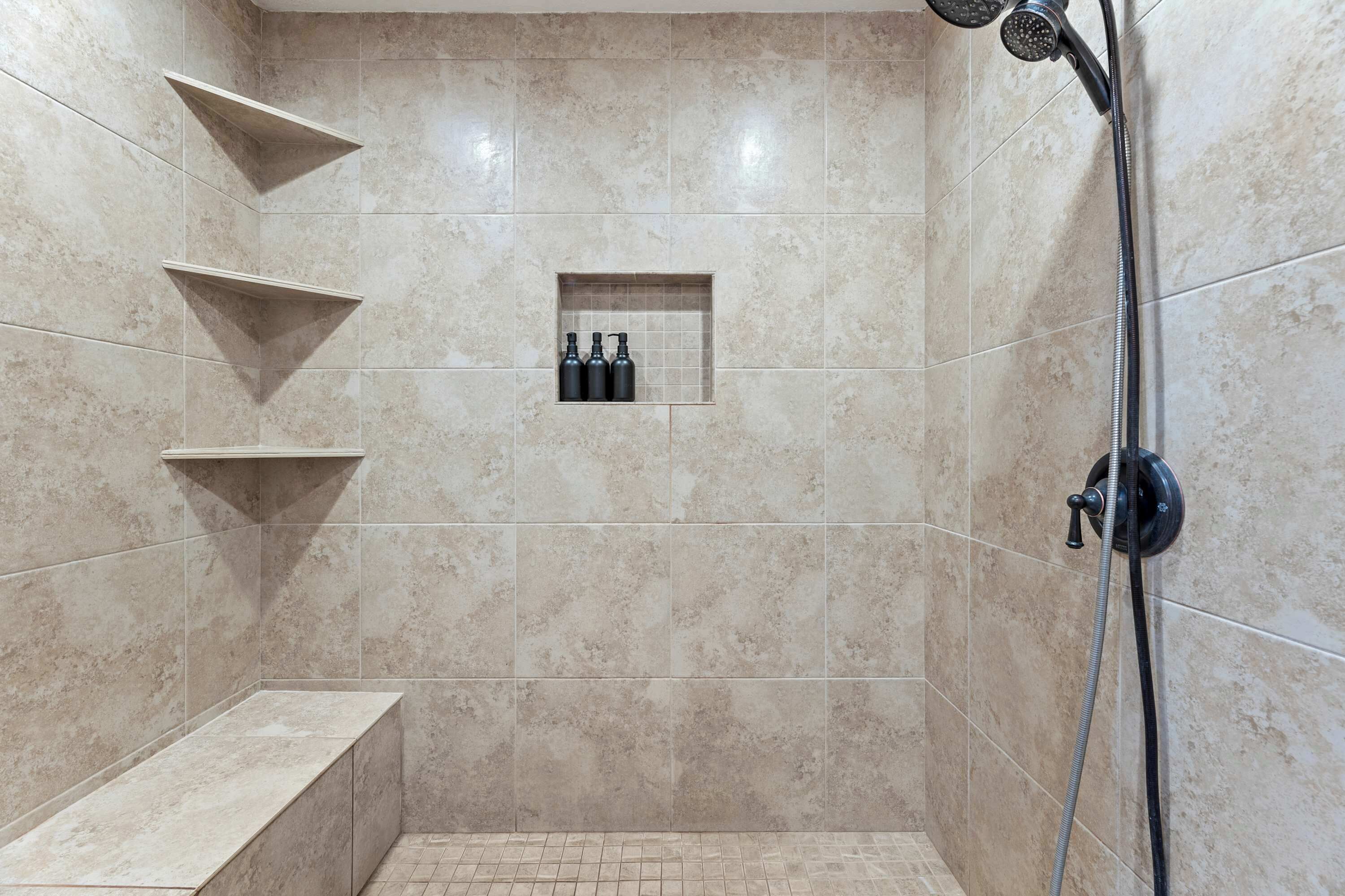 A shower area with beige tiles, a bench, and a shelf with bottles.