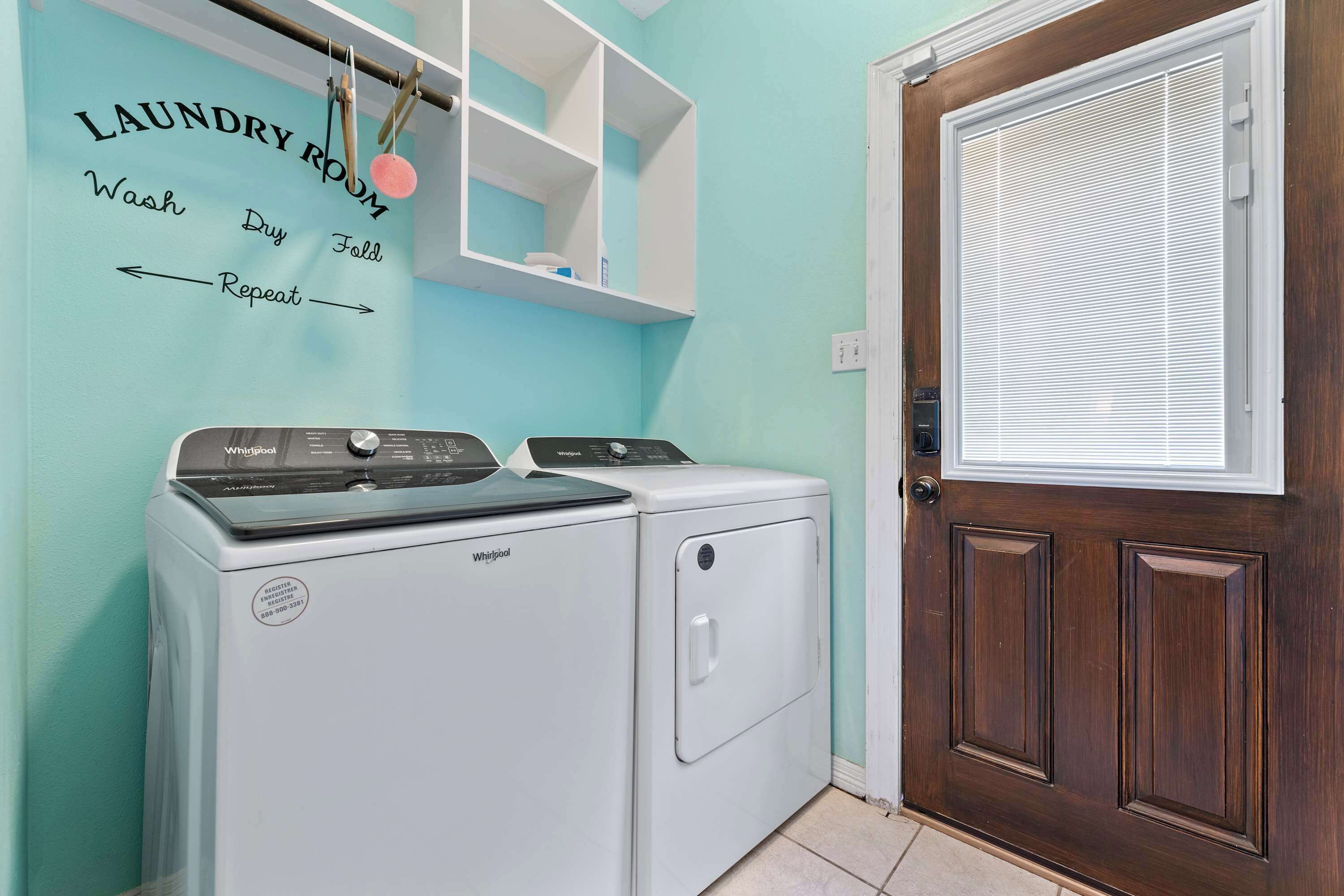 A laundry room with a Whirlpool washer and dryer, a wooden door, and a wall-mounted shelf with laundry instructions.