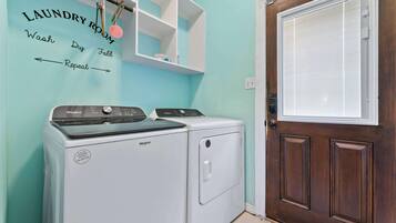 A laundry room with a Whirlpool washer and dryer, a wooden door, and a wall-mounted shelf with laundry instructions.