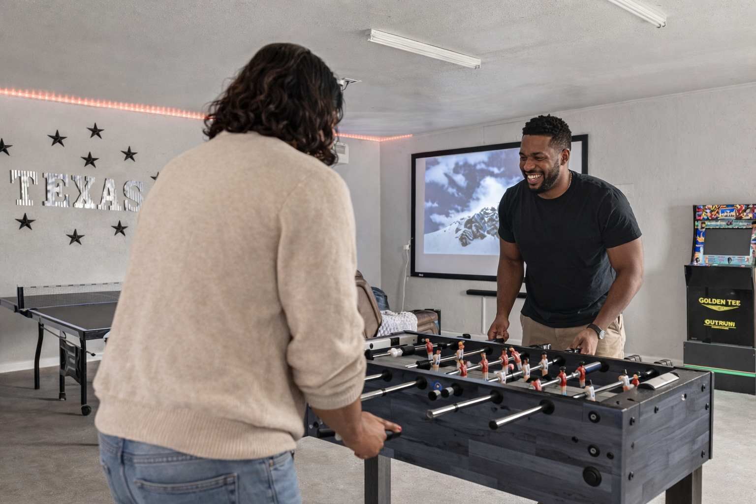 A room with a foosball table, a projector screen, and a wall with stars and the word 'TEXAS'.