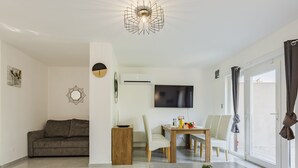 Un salon moderne comprenant un canapé, une table à manger avec des chaises, un téléviseur et une grande fenêtre avec des rideaux.