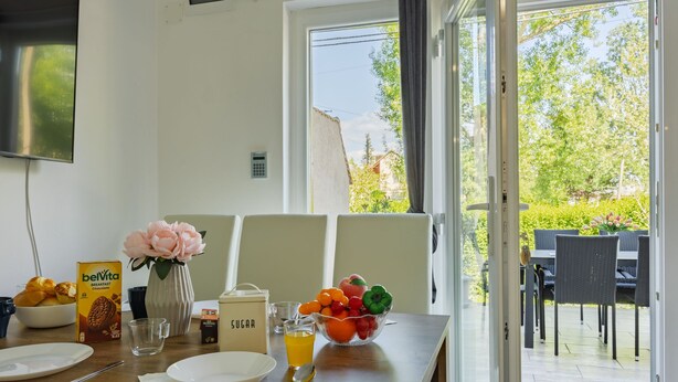Un coin repas avec une table mise pour le petit-déjeuner, comprenant un bol de fruits, un verre de jus d’orange et une boîte de croissants au chocolat de la marque Belvita.