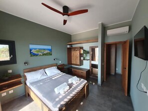 A bedroom with a bed, wooden headboard, bedside tables, a ceiling fan, a painting, a wardrobe, and a television. - Casa Bonita 2 Bedroom apt with the Best view in Town! (Palairos)
