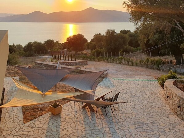A patio area with a stone floor, outdoor seating, and a view of a body of water and mountains in the distance. - Casa Bonita 2 Bedroom apt with the Best view in Town! (Palairos)