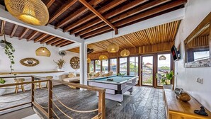 Un amplio espacio interior con mesa de billar, suelo de madera y una escalera.