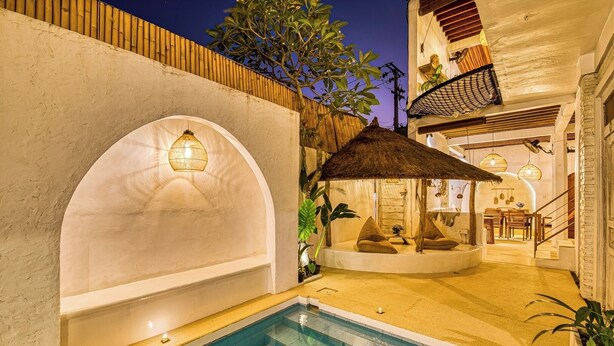 Zona de piscina con área de descanso cubierta por un techo de paja, una escalera que conduce a un nivel superior y vistas a la piscina.