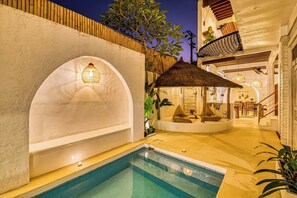 A pool area with a thatched roof seating area, a staircase leading to an upper level, and a view of the pool.