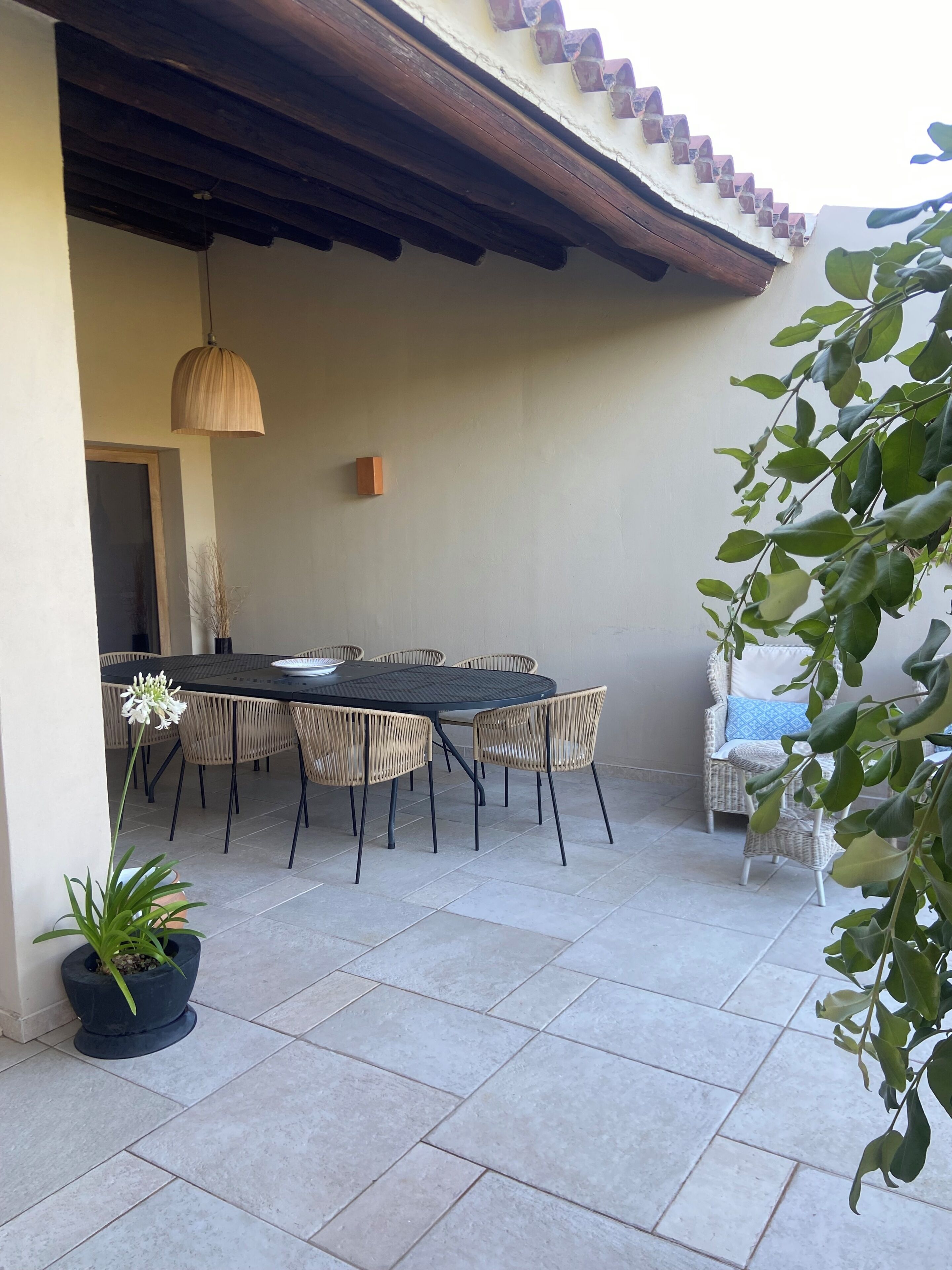 Un patio al aire libre con una mesa redonda y sillas, una lámpara colgante y una planta en maceta.