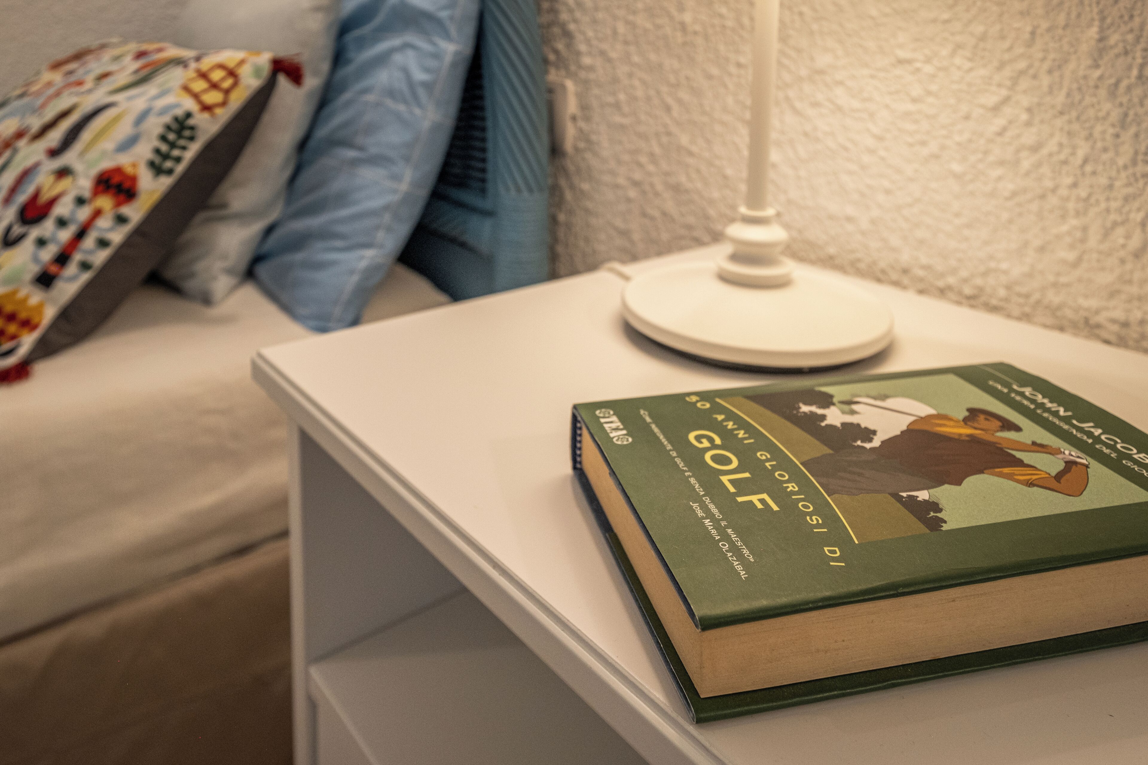 A book titled "Golf" on a white bedside table in a bedroom.