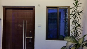 Μια είσοδος κατοικίας με μια ξύλινη πόρτα, ένα παράθυρο και αρκετά φυτά σε γλάστρες.