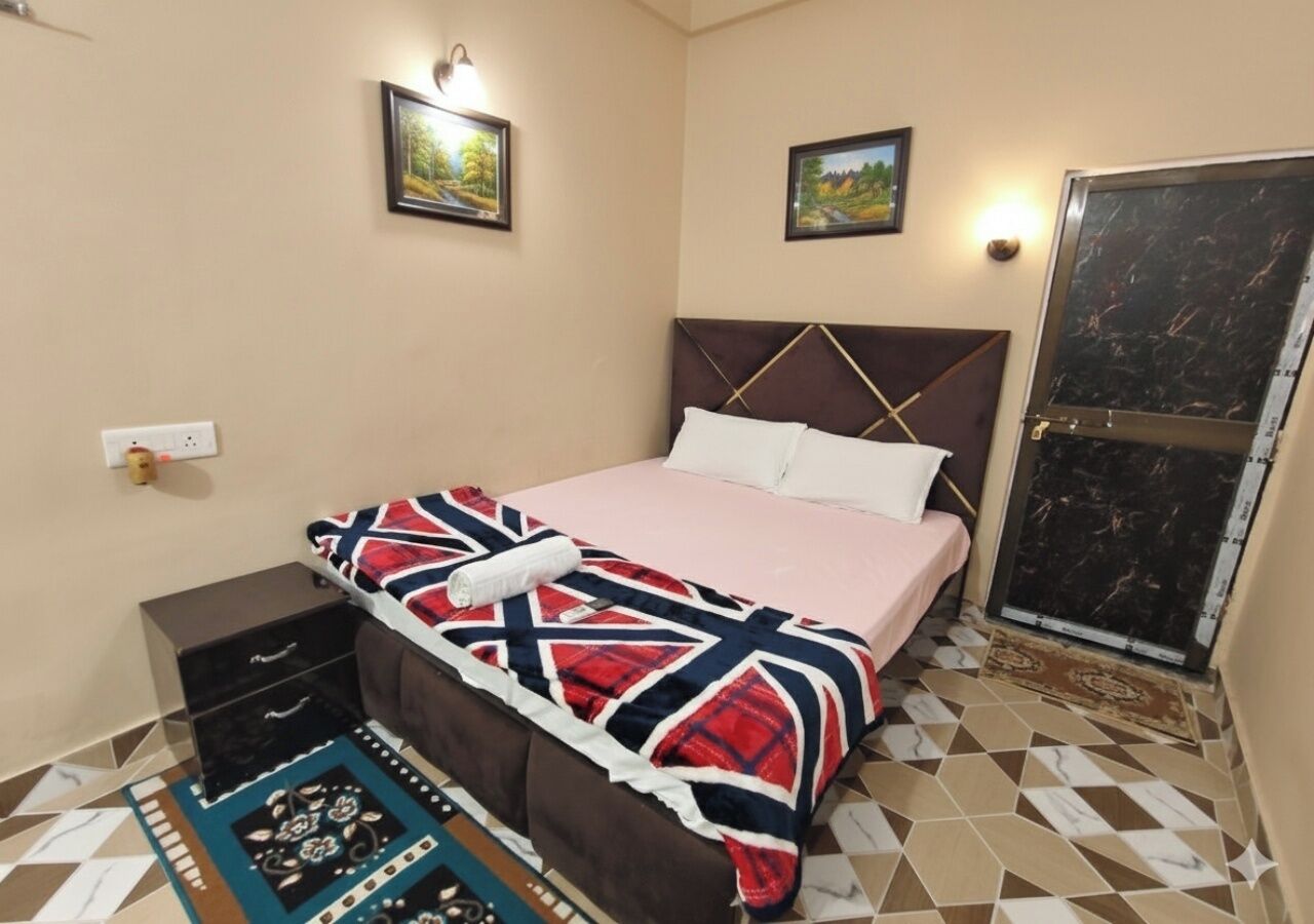 A bedroom with a bed, a nightstand, a dresser, a patterned rug, and two wall-mounted lights.
