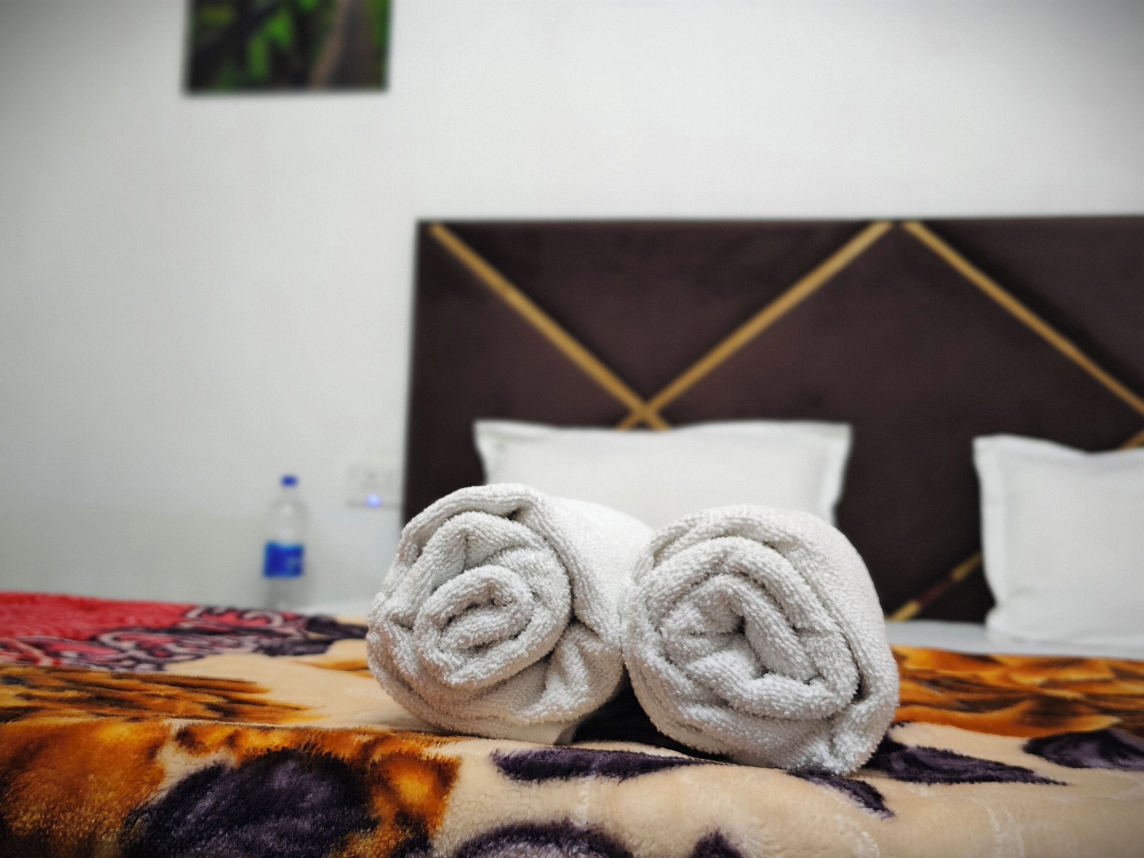 A neatly made bed with rolled towels, a patterned blanket, and a headboard with a geometric design.