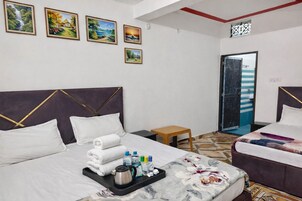 Una habitación de hotel con una cama, una mesita auxiliar, un taburete pequeño y una puerta que da a un balcón.