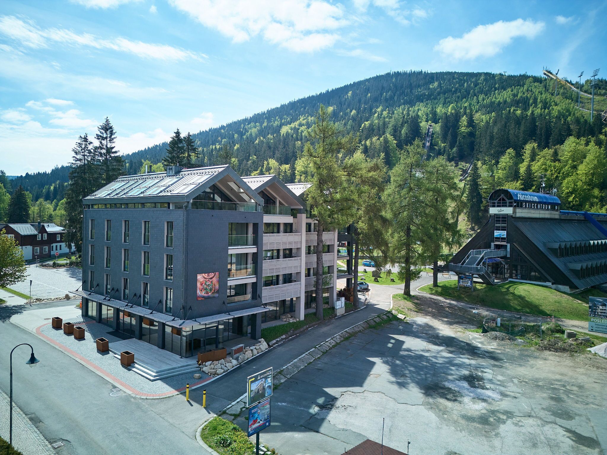 Un hôtel moderne à la façade en verre, avec de nombreux étages, et un centre de ski en arrière-plan.