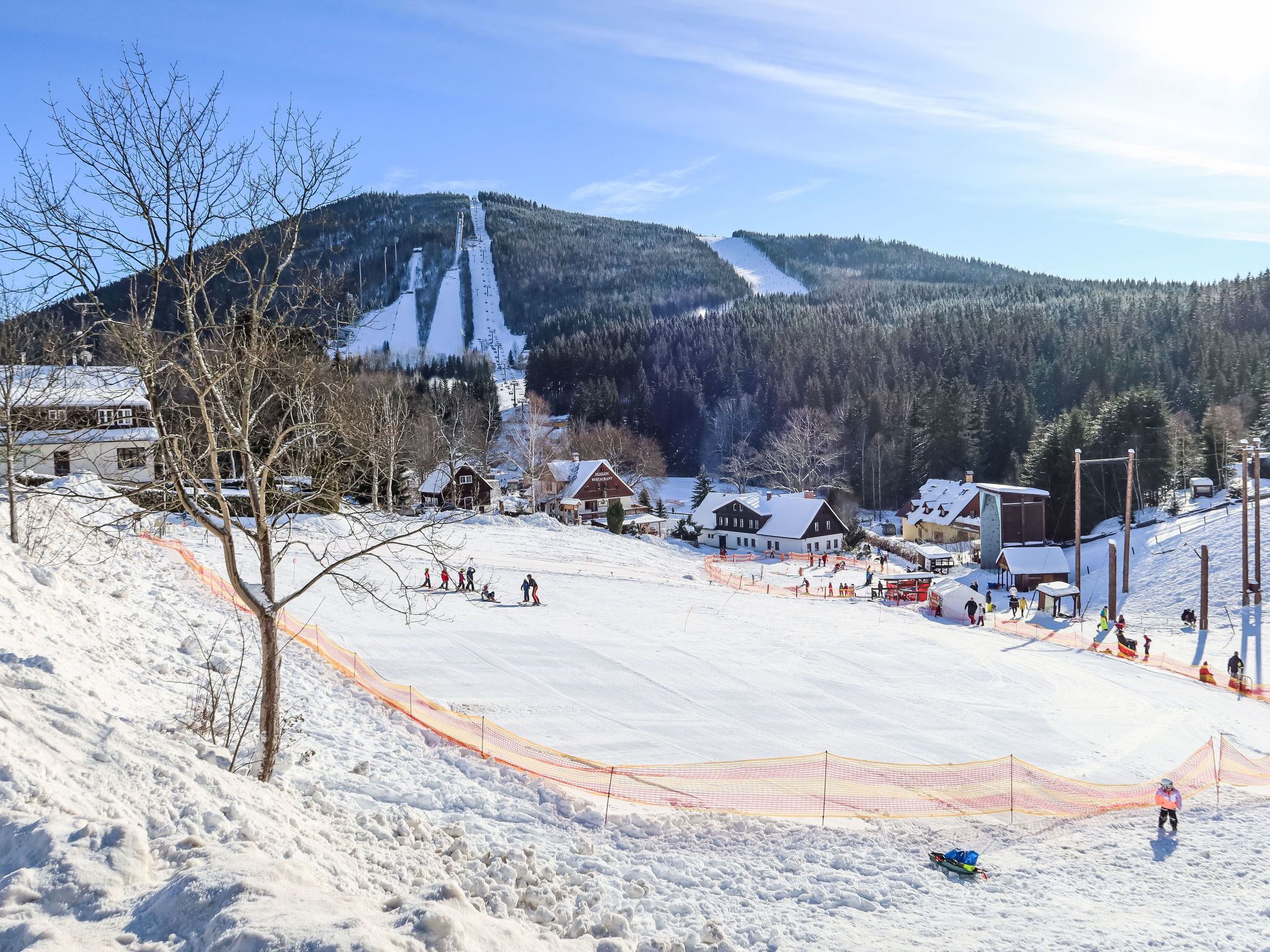 A snow-covered ski resort with a ski lift, buildings, and a mountain backdrop.