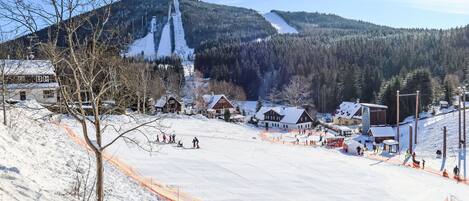 A snow-covered ski resort with a ski lift, buildings, and a mountain backdrop.