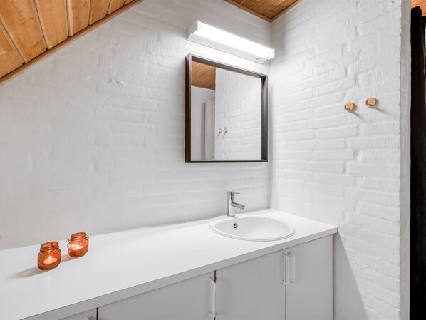 A modern bathroom with a white brick wall, a white sink, a mirror, and two candles on the countertop.