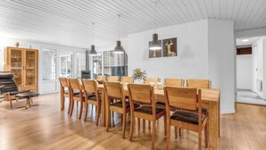 A spacious dining area with a long wooden table and chairs, white walls, and a high ceiling with exposed beams. - "Aagot" - 1.7km from the sea by Interhome (Ulfborg)
