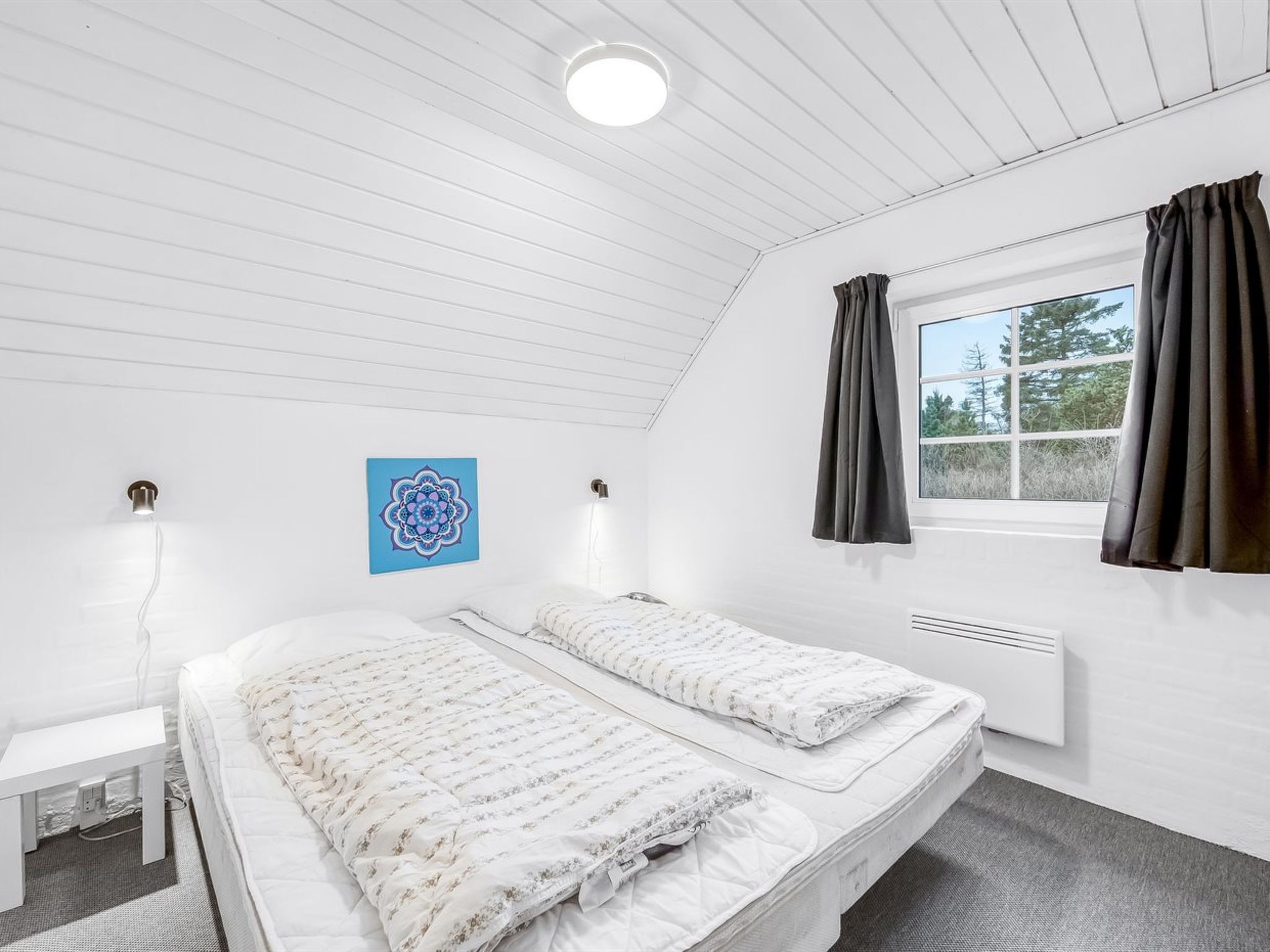 Une chambre à coucher comprenant un lit, un bureau, une fenêtre avec des rideaux, un radiateur et un luminaire au plafond.