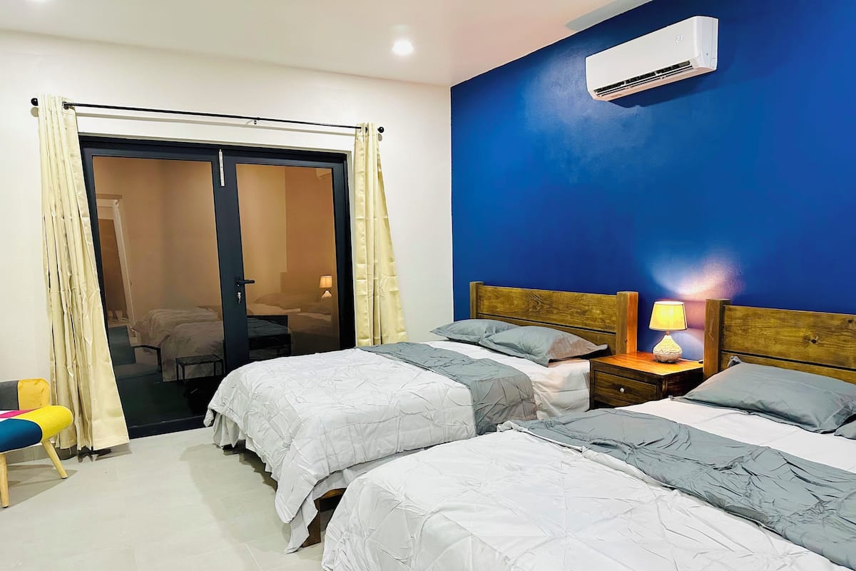 A hotel room with two beds, a sliding door, an air conditioning unit, and a nightstand with a lamp.