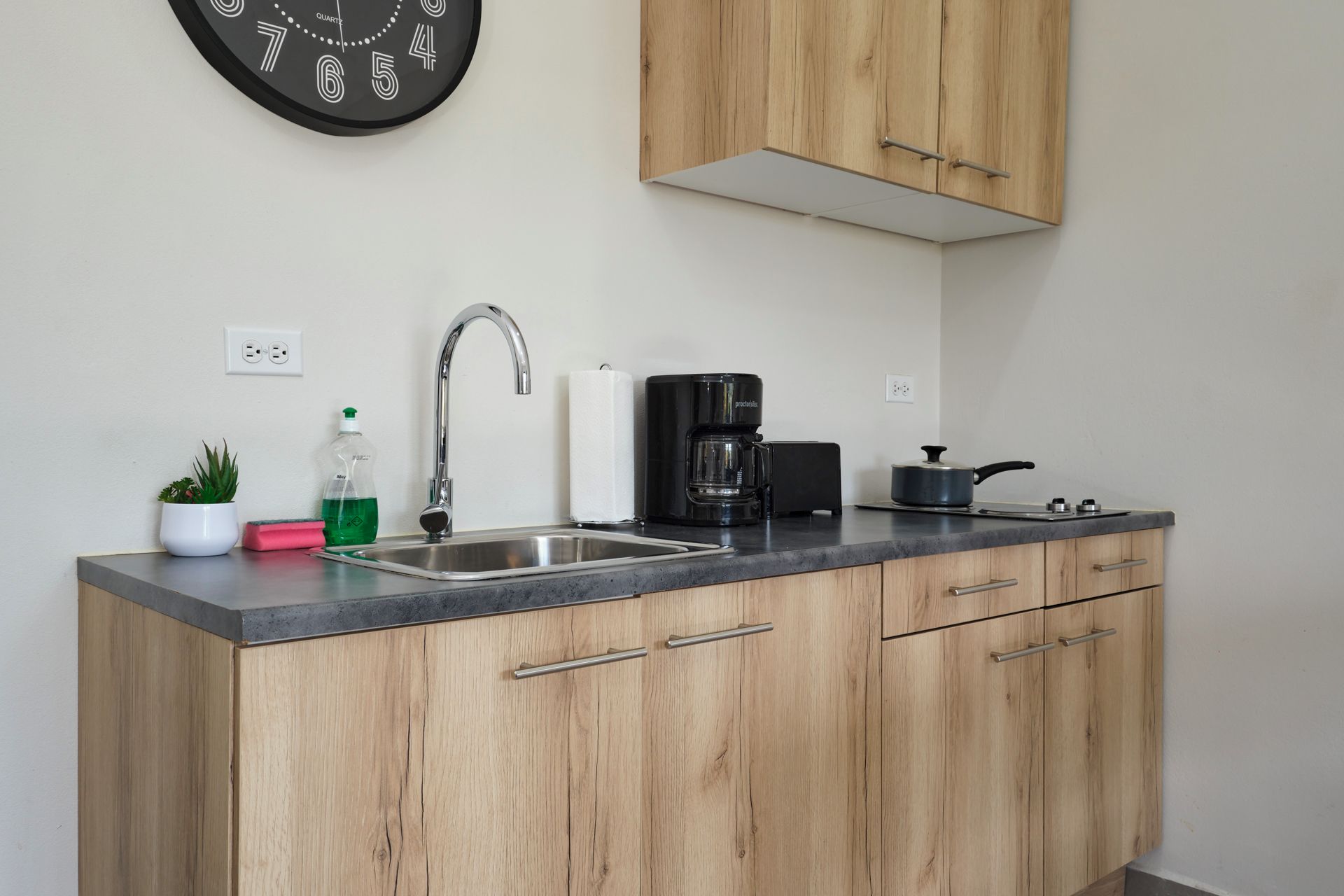 A kitchen with a stainless steel sink, a coffee maker, and wooden cabinets.