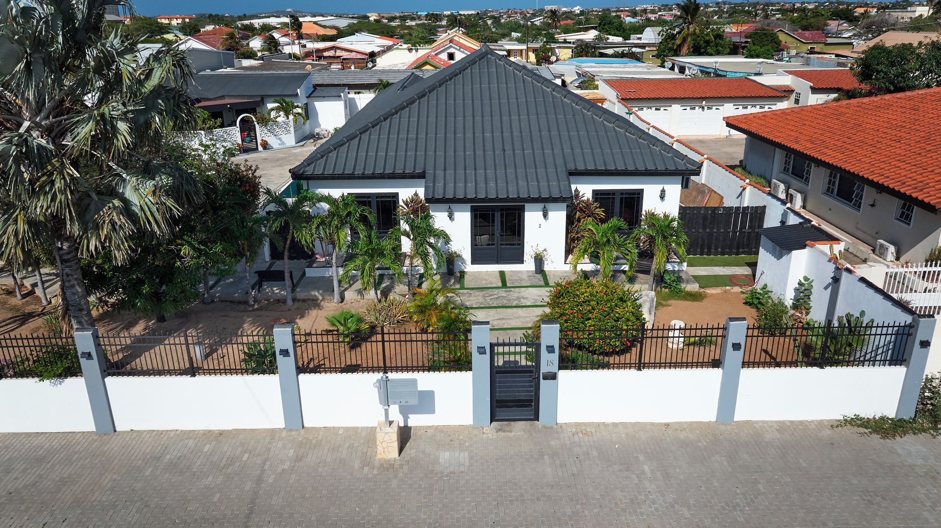 Un barrio residencial con una casa que tiene techo oscuro, paredes blancas y una entrada protegida por una reja.
