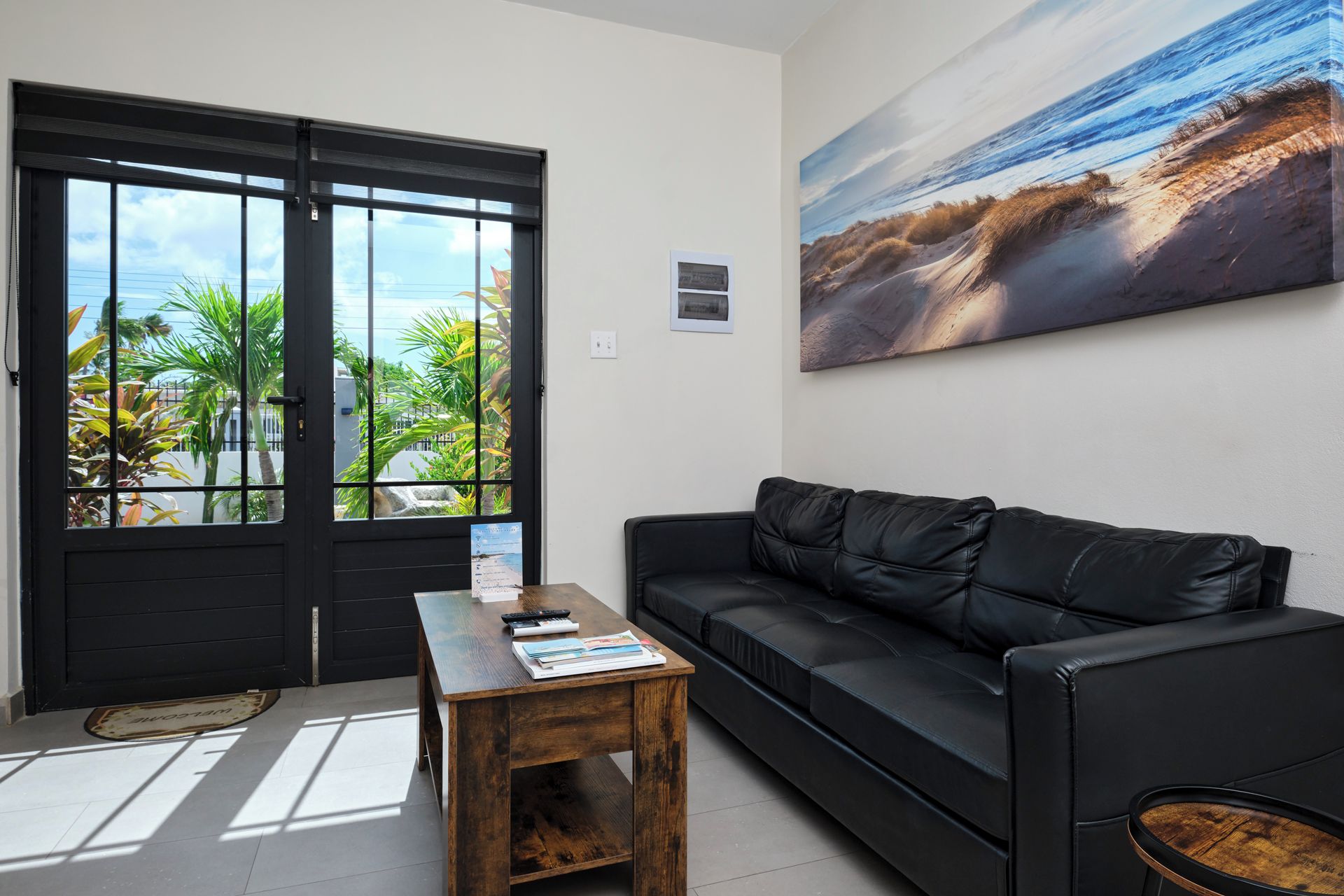 A living room with a black leather sofa, a wooden coffee table, and a large beach painting on the wall.