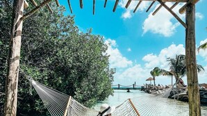 A hammock under a wooden pergola on a beach with clear water and lush greenery. - Eagle Stays Aruba (Oranjestad)