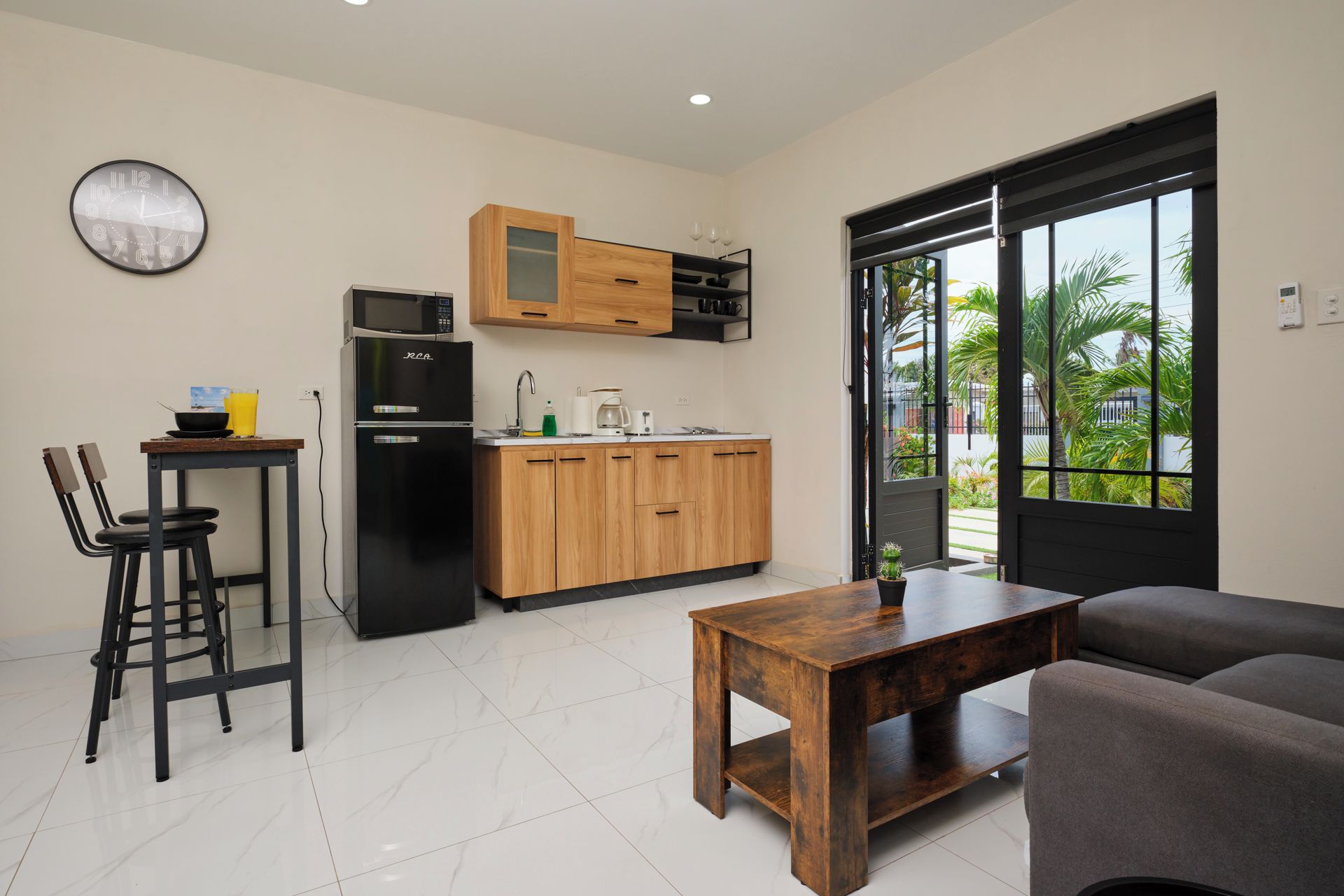 Eine moderne Küche mit Kühlschrank, Mikrowelle und Holzschränken. Ein Essbereich mit Tisch und Stühlen lädt zum Verweilen ein, und ein großes Fenster bietet einen Blick ins Freie.