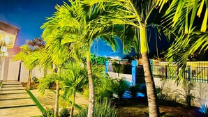 A well-lit residential area with palm trees, a concrete pathway, and a house with a blue facade. - Eagle Stays Aruba (Oranjestad)
