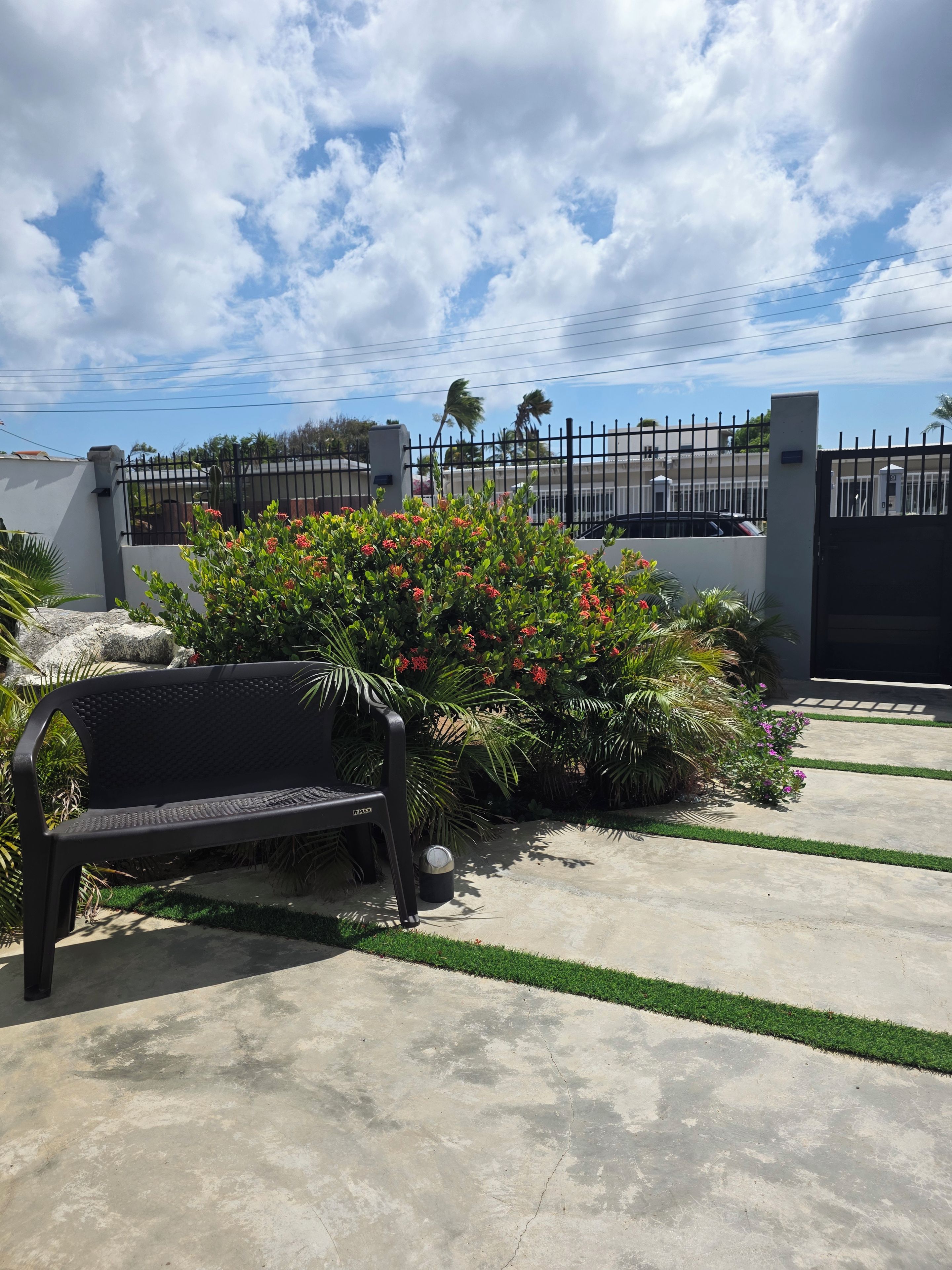 A paved outdoor area with a bench, a black gate, and a fence.